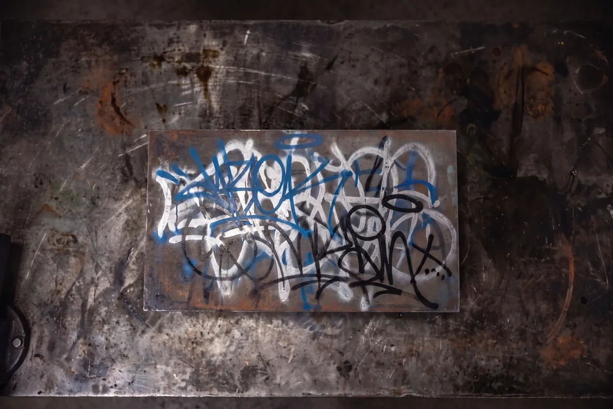 Steel panel covered in spray paint graffiti tags before laser removal