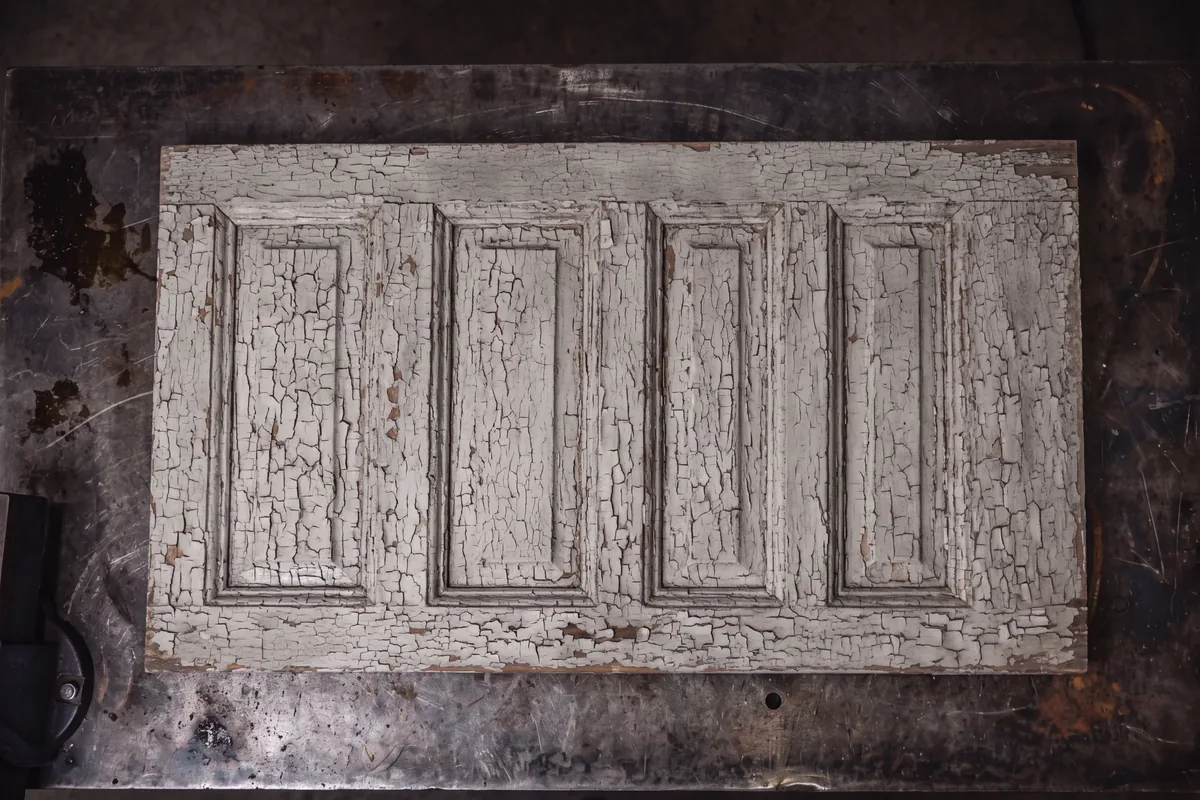 Antique oak door panel under layers of cracked white paint before laser stripping